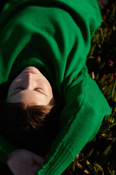 Model lying down with arms raised wearing a kelly green cropped guernsey