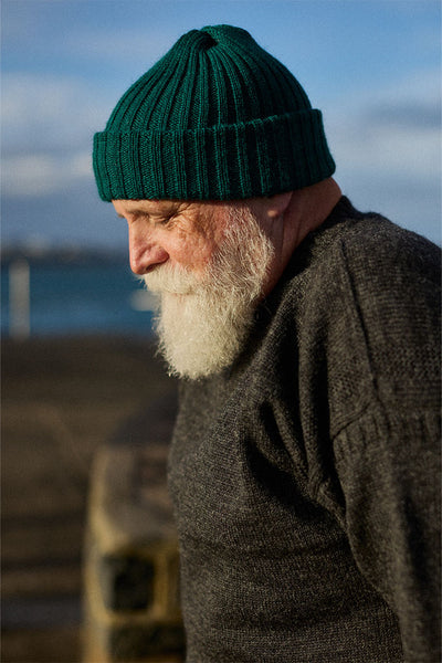 Man wearing a green knit beanie and dark sweater by a body of water.